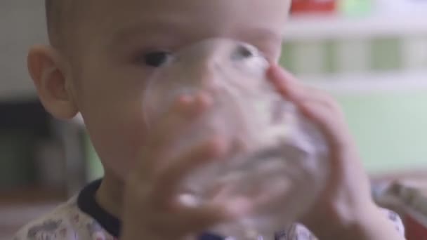 子供は水を飲む 面白い混合レース2歳の赤ちゃんの少年は 水のガラスを保持し 飲みしようとしています 選択的焦点 — ストック動画