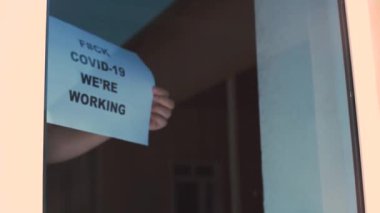 Shop or restaurant worker hanging a paper with warning - Fuck covid-19, We are working. Restarant begin working after coronavirus or covid-19 pandemic