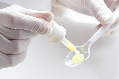 Eczacı, pipet ve kaşıkla öksürük şurubu dozu yapıyor.