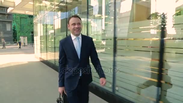 Un uomo d'affari felice in giacca e cravatta che cammina per strada, guardando l'orologio. Steadicam shot . — Video Stock