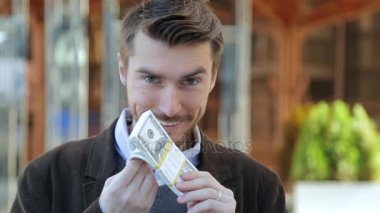 Dolar bir demet leafing, nakit kokulu, kameraya bakıyor ve gülümsüyor çekici adam