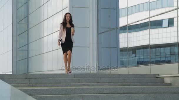 Hübsches Mädchen mit einer Tasse Kaffee, das auf Stöckelschuhen die Straße hinunterläuft. Steadicam-Aufnahme. — Stockvideo