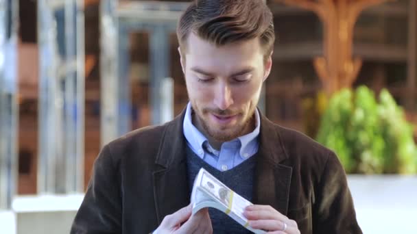 Attraktiver Mann blättert durch ein Bündel Dollars, blickt in die Kamera und lächelt — Stockvideo