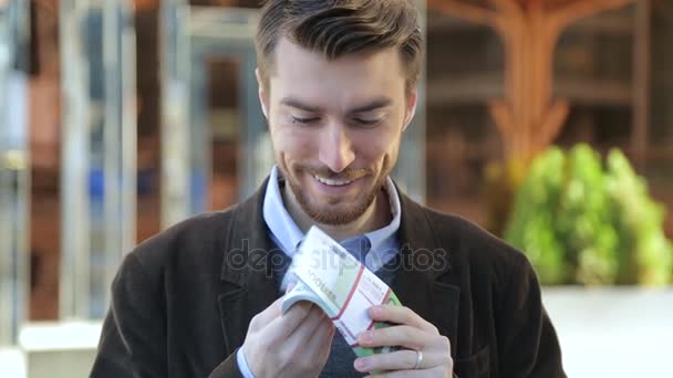 Uomo attraente sfogliando un fascio di euro, guardando la fotocamera e sorridendo — Video Stock