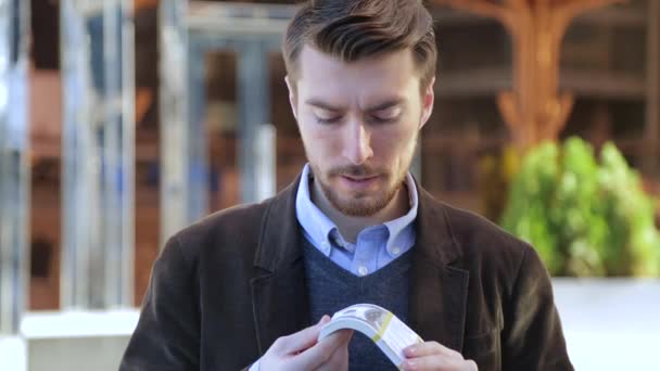 Hombre atractivo hojeando a través de un paquete de dólares, mirando a la cámara y sonriendo — Vídeos de Stock