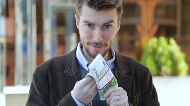 Привлекательный мужчина листает пачку евро, смотрит в камеру и улыбается — стоковое видео