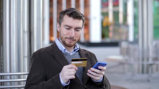 Aantrekkelijke man met behulp van online bankieren op smartphone met credit card in de straat (schuifknop schot) — Stockvideo