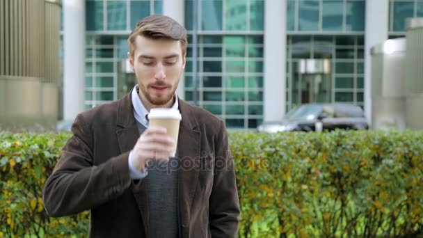Uomo attraente che beve caffè o tè dalla tazza di carta, guardando la fotocamera, sorridendo — Video Stock