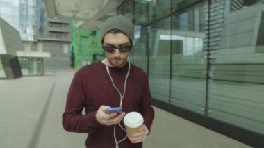 App kullanarak ve akıllı telefon kulaklık müzik dinlemek, kahve içme ve yürüme yakışıklı hipster
