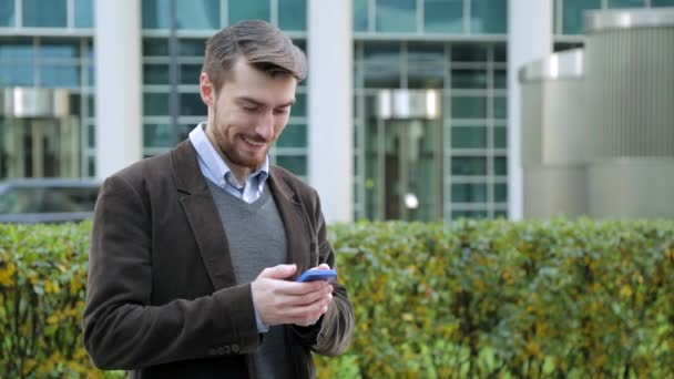 Hombre atractivo utilizando la aplicación en el teléfono inteligente, sonriendo — Vídeos de Stock