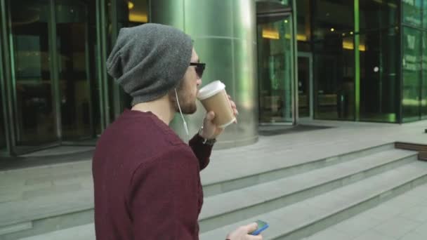 Belle hipster utilisant l'application et écouter de la musique dans les écouteurs smartphone, boire du café et marcher Vidéo De Stock Libre De Droits