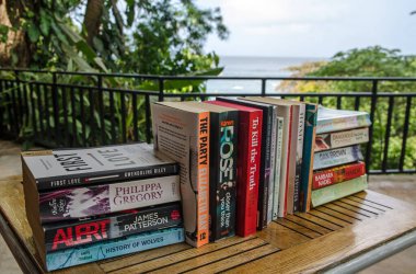 Castara, Trinidad and Tobago - January 12, 2020:  A selection of popular paperback fiction books sitting on a terrace overlooking the Caribbean sea. clipart