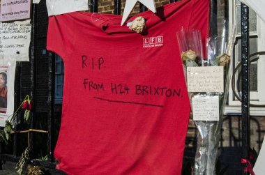 LONDON, İngiltere - 5 Temmuz 2017: Kensington, Londra 'daki Grenfell Tower yangınının kurbanlarının anıları. Çiçekler ve mesajlar arasında Londra İtfaiyesi 'nin Brixton İtfaiyesi' nden itfaiyecilerin gönderdiği bir tişört de var..