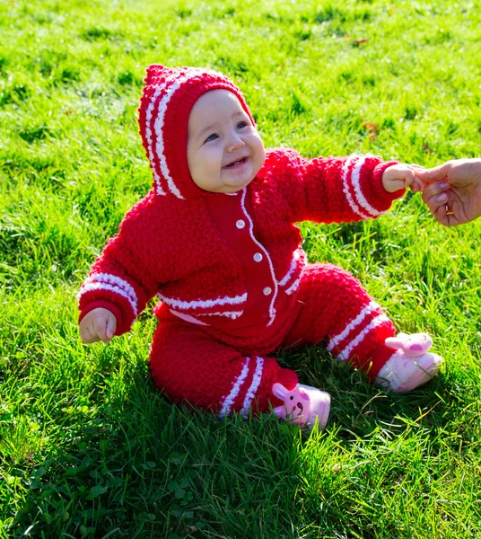 Little baby sitting on the grass. Mom holding the baby by the arm — Stock Photo, Image