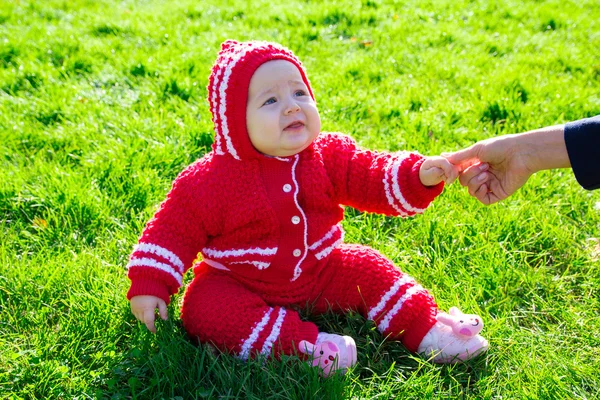 Маленька дитина сидить на траві. Мама тримає дитину за руку — стокове фото