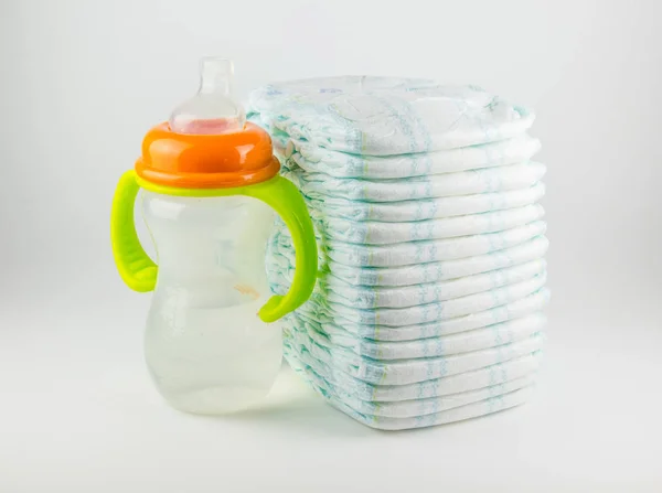 Fraldas para bebês e garrafa em um fundo branco — Fotografia de Stock