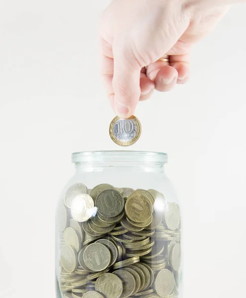 Glass jar with money on a white background. Hand with a coin