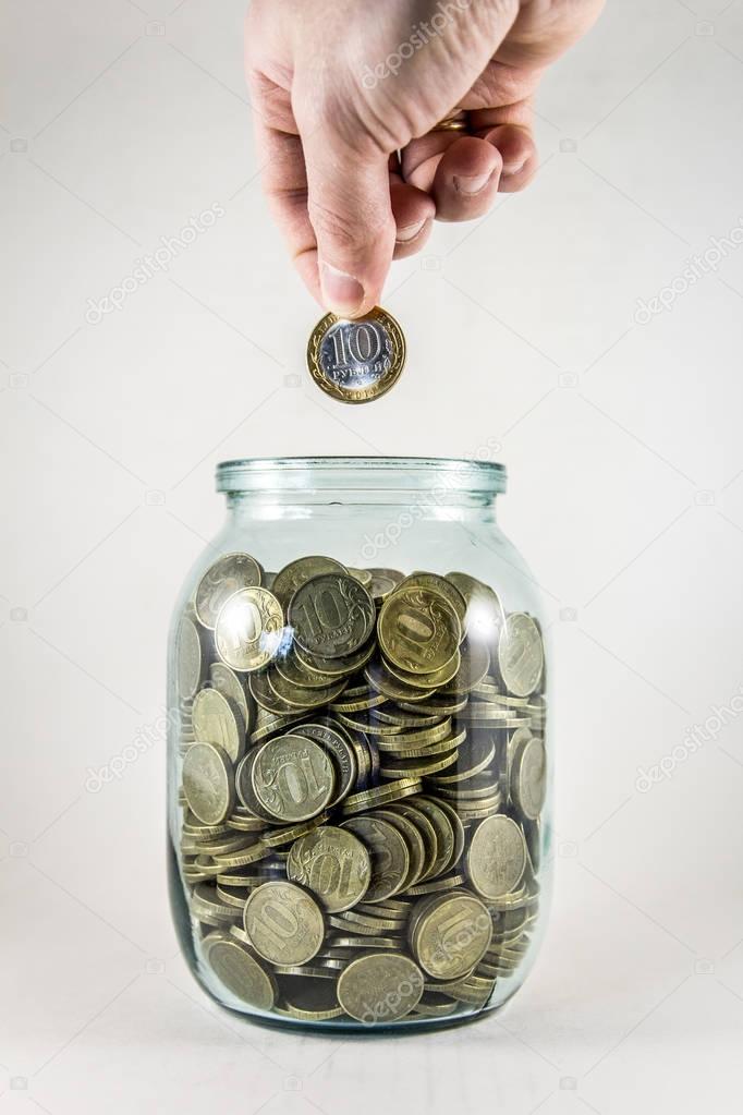 Glass jar with money on a white background. Hand with a coin