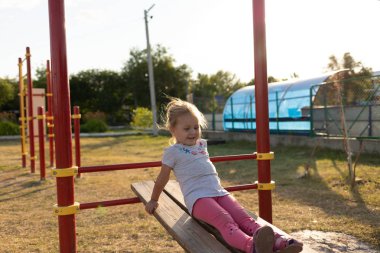 Küçük bir çocuk stadyuma spor için gider. Yatay çubukta asılı, eğri büğrü parmaklıklarda.