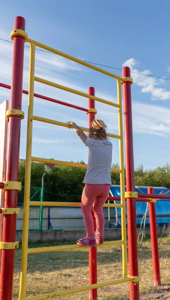 Küçük bir çocuk stadyuma spor için gider. Yatay çubukta asılı, eğri büğrü parmaklıklarda.