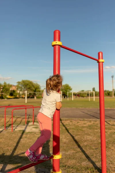 Un niño pequeño va a practicar deportes en el estadio. colgando en la barra horizontal, en las barras irregulares —  Fotos de Stock