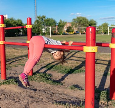 Küçük bir çocuk stadyuma spor için gider. Yatay çubukta asılı, eğri büğrü parmaklıklarda.