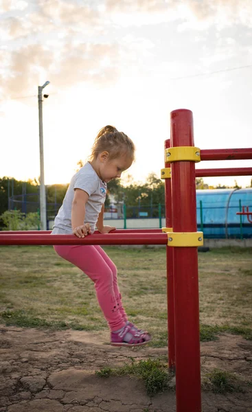 Un niño pequeño va a practicar deportes en el estadio. colgando en la barra horizontal, en las barras irregulares —  Fotos de Stock