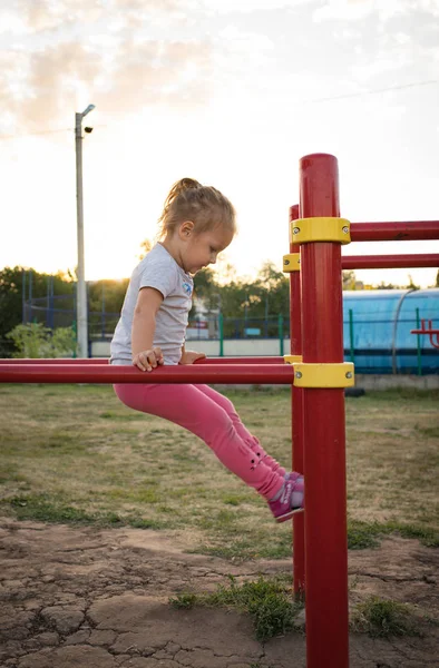 Un niño pequeño va a practicar deportes en el estadio. colgando en la barra horizontal, en las barras irregulares —  Fotos de Stock