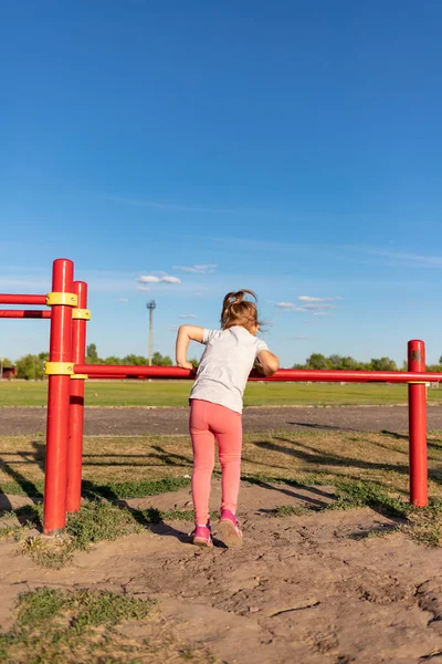 Un niño pequeño va a practicar deportes en el estadio. colgando en la barra horizontal, en las barras irregulares —  Fotos de Stock