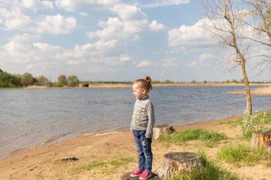 Çocuk bir kütüğün üzerinde duruyor, uzaklığa bakıyor.