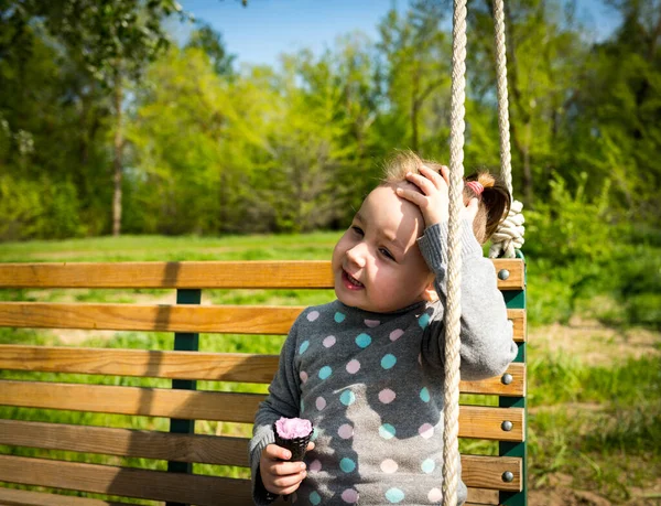 Dítě jí zmrzlinu v černém vaflovacím kuželu sedící na houpačce — Stock fotografie