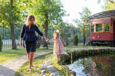 Anne ve kızı parkta el ele tutuşuyorlar.