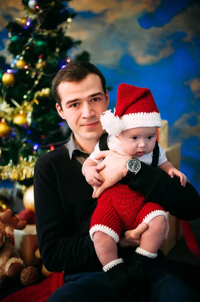 Χαριτωμένο μικρό αγόρι και ο πατέρας του καθισμένος στο χριστουγεννιάτικο δέντρο — Φωτογραφία Αρχείου