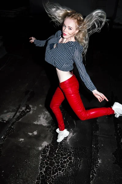 Outdoor Portret van mooie gelukkig blond Europese jongedame poseren op straat 's nachts. Model dragen van stijlvolle kleding rode broek en springen. Vrouwelijke mode. Stad nacht levensstijl. Kopiëren van ruimte. — Stockfoto