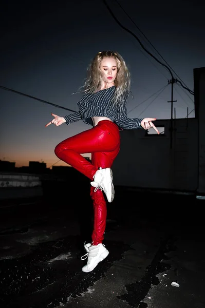 Outdoor Portret van mooie gelukkig blond Europese jongedame poseren op straat 's nachts. Model dragen van stijlvolle kleding rode broek en springen. Vrouwelijke mode. Stad nacht levensstijl. Kopiëren van ruimte. — Stockfoto