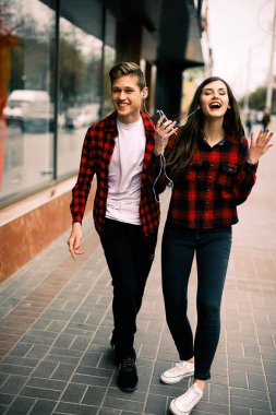 Kulaklık ile müzik dinlemek, birbirlerine söz ve gülümseyen yürüyüş ve şehirde dans iki mutlu trendy genç arkadaş. Yaşam tarzı, dostluk ve kentsel yaşam kavramları.