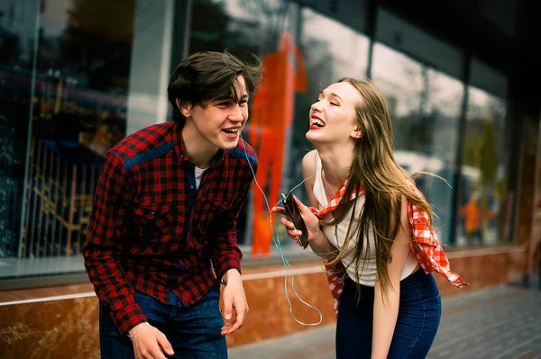 Zwei fröhliche trendige Teenager-Freunde, die durch die Stadt spazieren und tanzen, die Musik mit Kopfhörern hören, miteinander reden und lächeln. Lebensstil, Freundschaft und urbane Lebenskonzepte. — Stockfoto