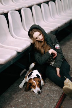 Genç hippi kız oynamak, junping ve sarılma ve açık eski stadyumda eğlenmek evde beslenen hayvan Estonya tazı köpeği ile.