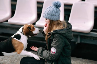 Genç hippi kız oynamak, junping ve sarılma ve açık eski stadyumda eğlenmek evde beslenen hayvan Estonya tazı köpeği ile.