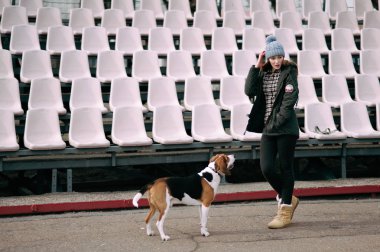 Genç hippi kız oynamak, junping ve sarılma ve açık eski stadyumda eğlenmek evde beslenen hayvan Estonya tazı köpeği ile.