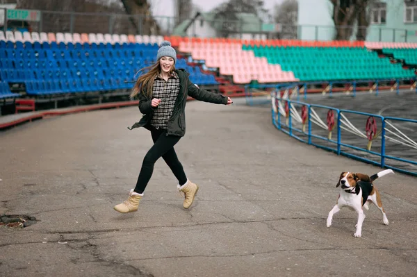 Fiatal csípő lány vele kisállat észt kutya kutya játék, Terézia, és átölelve, és birtoklás móka szabadtéri, a régi stadion. — Stock Fotó