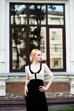 Mutlu moda sarışın Avrupa zarif kadın kırmızı dudakları ve beyaz ayakta yeşil çimenlerin üzerinde bina eski kırmızı tuğla, Cilt. Seksi kız açık havada. Resmi siyah beyaz elbiseli güzel kadın.