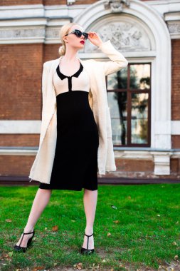 Mutlu moda sarışın Avrupa zarif kadın kırmızı dudakları ve beyaz ayakta yeşil çimenlerin üzerinde bina eski kırmızı tuğla, Cilt. Seksi kız açık havada. Resmi siyah beyaz elbiseli güzel kadın 