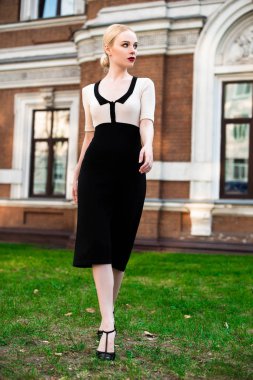 Mutlu moda sarışın Avrupa zarif kadın kırmızı dudakları ve beyaz ayakta yeşil çimenlerin üzerinde bina eski kırmızı tuğla, Cilt. Seksi kız açık havada. Resmi siyah beyaz elbiseli güzel kadın.