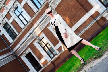 Mutlu moda sarışın Avrupa zarif kadın kırmızı dudakları ve beyaz ayakta yeşil çimenlerin üzerinde bina eski kırmızı tuğla, Cilt. Seksi kız açık havada. Resmi siyah beyaz elbiseli güzel kadın 