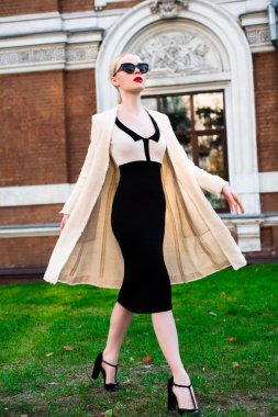 Mutlu moda sarışın Avrupa zarif kadın kırmızı dudakları ve beyaz ayakta yeşil çimenlerin üzerinde bina eski kırmızı tuğla, Cilt. Seksi kız açık havada. Resmi siyah beyaz elbiseli güzel kadın 