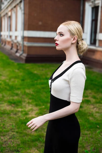 Mutlu moda sarışın Avrupa zarif kadın kırmızı dudakları ve beyaz ayakta yeşil çimenlerin üzerinde bina eski kırmızı tuğla, Cilt. Seksi kız açık havada. Resmi siyah beyaz elbiseli güzel kadın.