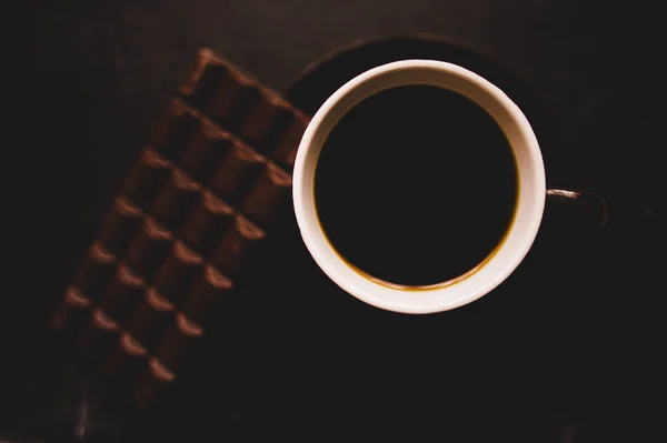 Taza de café con granos y chocolate sobre mesa de madera sobre fondo oscuro — Foto de Stock