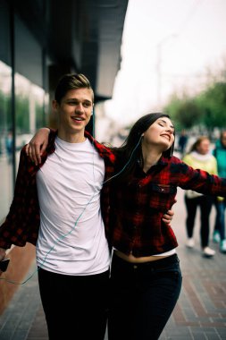 Kulaklık ile müzik dinlemek, birbirlerine söz ve gülümseyen yürüyüş ve şehirde dans iki mutlu trendy genç arkadaş. Yaşam tarzı, dostluk ve kentsel yaşam kavramları.