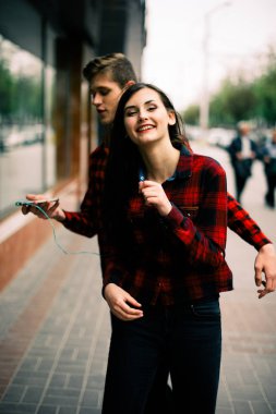 Kulaklık ile müzik dinlemek, birbirlerine söz ve gülümseyen yürüyüş ve şehirde dans iki mutlu trendy genç arkadaş. Yaşam tarzı, dostluk ve kentsel yaşam kavramları.